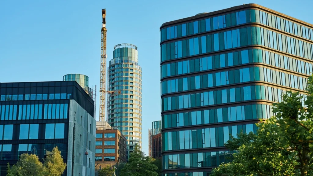 Modern glass buildings with a crane beside a cylindrical tower under construction.